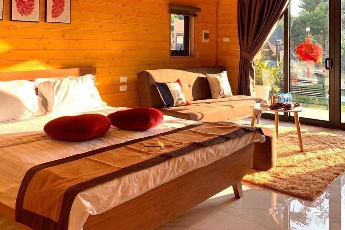 Ein Schlafzimmer einer Holzhütte mit einem großen Bett, einem kleinen Tisch und Blick ins Freie.