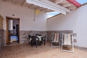 A covered patio area with a table and chairs, a bed in the background, and a brick wall.