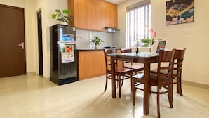 A modern kitchen with wooden cabinets, a black refrigerator, and a dining table with chairs. - Quan Nhan Apartment (Hanoi)