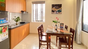 A modern kitchen with wooden cabinets, a built-in stove, and a dining area with a glass table and chairs. - Quan Nhan Apartment (Hanoi)