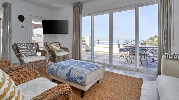 Ruime kamer met een groot bed, twee rieten stoelen, een bank en een balkon met een tafel en stoelen.