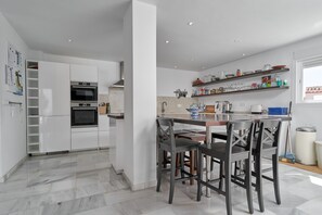 Une cuisine moderne avec des meubles blancs, un four encastré et un coin repas comprenant une table et des chaises.