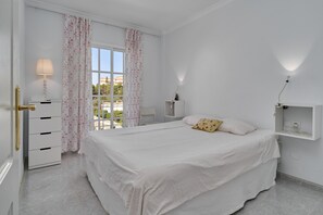 Une chambre à coucher avec un lit, une table de chevet, une lampe, une fenêtre avec des rideaux et une vue sur l’extérieur.