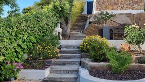 Un escalier en pierre mène à un bâtiment à la façade en pierre, qui est entouré de différentes plantes et fleurs.