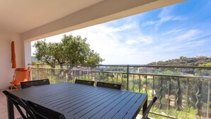 Un balcon avec une table et des chaises, une vue sur la verdure et les bâtiments, et un ciel dégagé.