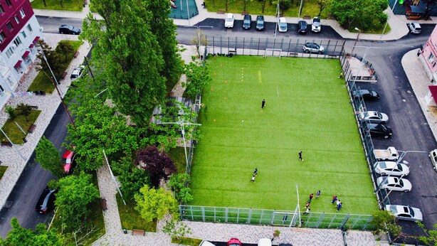 Ett flygbildsfoto av en parkeringsplats som ligger intill en fotbollsplan, där flera bilar är parkerade.