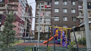En lekplats med en rutschkana och klätterställningar, omgiven av flerfamiljshus med balkonger och tvätt som hänger på tork.