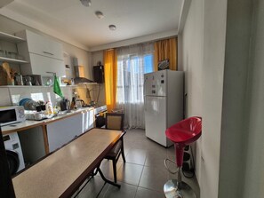 A compact kitchen with a dining table, a red bar stool, a washing machine, and a refrigerator. - Cosy & Stylish with garden view (Batumi)