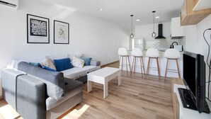 En moderne stue med en grå sofa, et hvidt sofabord og et køkkenområde med en sort emfang.