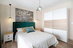 Une chambre à coucher avec un lit, deux tables de chevet, une commode, un tableau au mur et une grande fenêtre donnant sur un beau paysage.