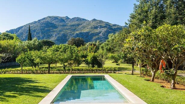 A rectangular pool with a clear blue water surface, surrounded by well-maintained grass and trees, with a mountainous backdrop. - Villa 'Alfonsa' with Mountain View, Wi-Fi and Air Conditioning (pollensa)