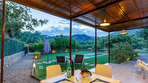 An outdoor dining area with a table set for two, surrounded by chairs, and overlooking a garden with a view of hills. - Villa 'Alfonsa' with Mountain View, Wi-Fi and Air Conditioning (pollensa)
