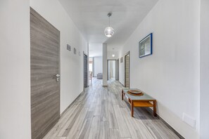 Un couloir avec une porte en bois, un banc surmonté d’un panier en osier et des œuvres d’art encadrées accrochées aux murs.