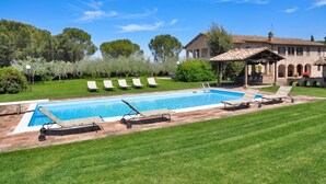 A swimming pool with lounge chairs, a covered patio, and a building with arches. - Villa del Colle (Torgiano)