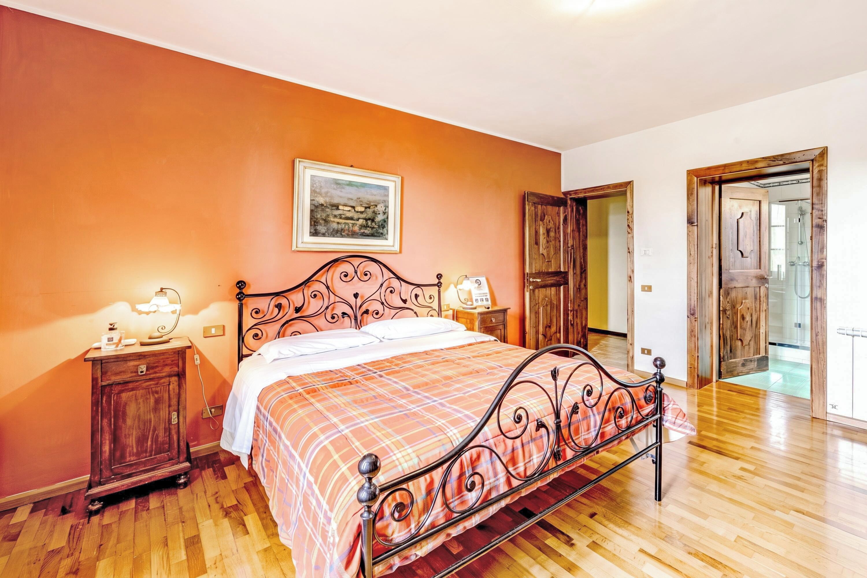 Un dormitorio con cama, mesitas de noche, un armario de madera y una puerta que da a otra habitación.