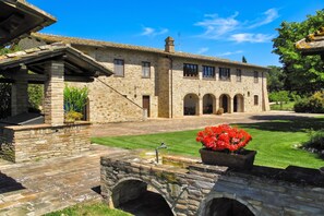 A stone building with a tiled roof, a stone archway, and a well-maintained lawn. - Villa del Colle (Torgiano)