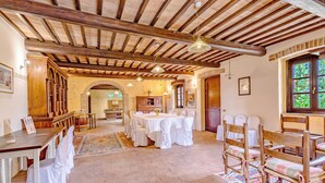 A spacious dining area with wooden tables and chairs, a high ceiling with exposed beams, and a view through a window. - Villa del Colle (Torgiano)