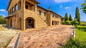 A stone building with a courtyard, arched windows, and a bicycle. - Villa del Colle (Torgiano)