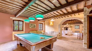 A pool table in a room with exposed wooden beams and stone walls. - Villa del Colle (Torgiano)
