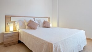 Un letto rifatto con cura, con una testiera in legno, un comodino con una lampada e una cassettiera.