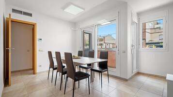 Un comedor moderno con una mesa y sillas, un vidrio corredero hacia un balcón y vistas de edificios.