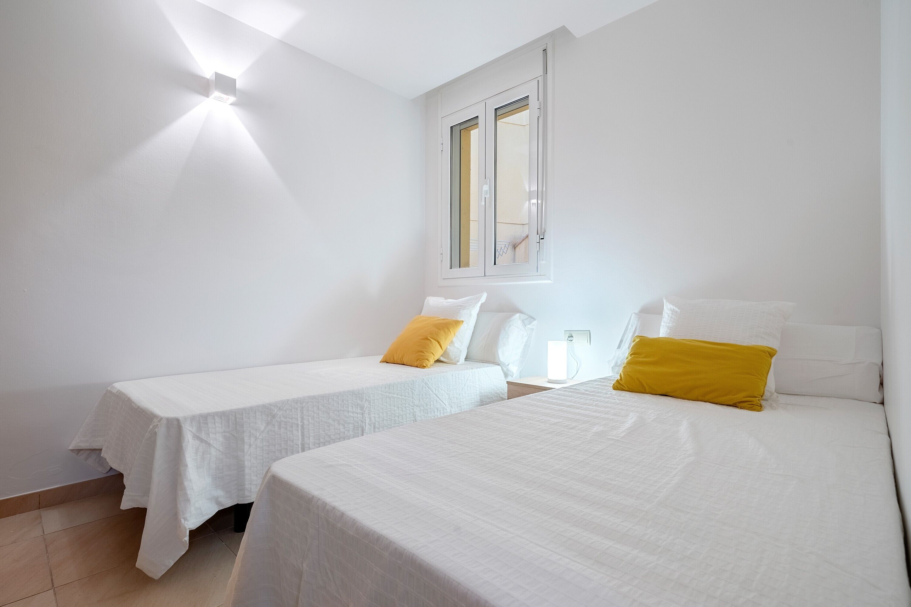 Una habitación con dos camas, una ventana y una lámpara.