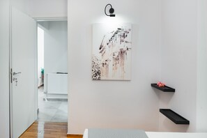 Ein modernes Zimmer mit einer weißen Tür, einem zur Küche führenden Gang, einer wandmontierten Lampe und einem gerahmten Kunstwerk.