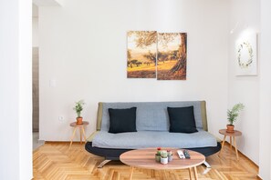 Ein modernes Wohnzimmer mit einem grauen Sofa, zwei Beistelltischen mit Pflanzen, einem runden Couchtisch und zwei an der Wand befestigten Kunstwerken.