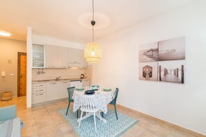 Une cuisine moderne avec des meubles blancs, une table à manger avec des chaises et un luminaire suspendu.