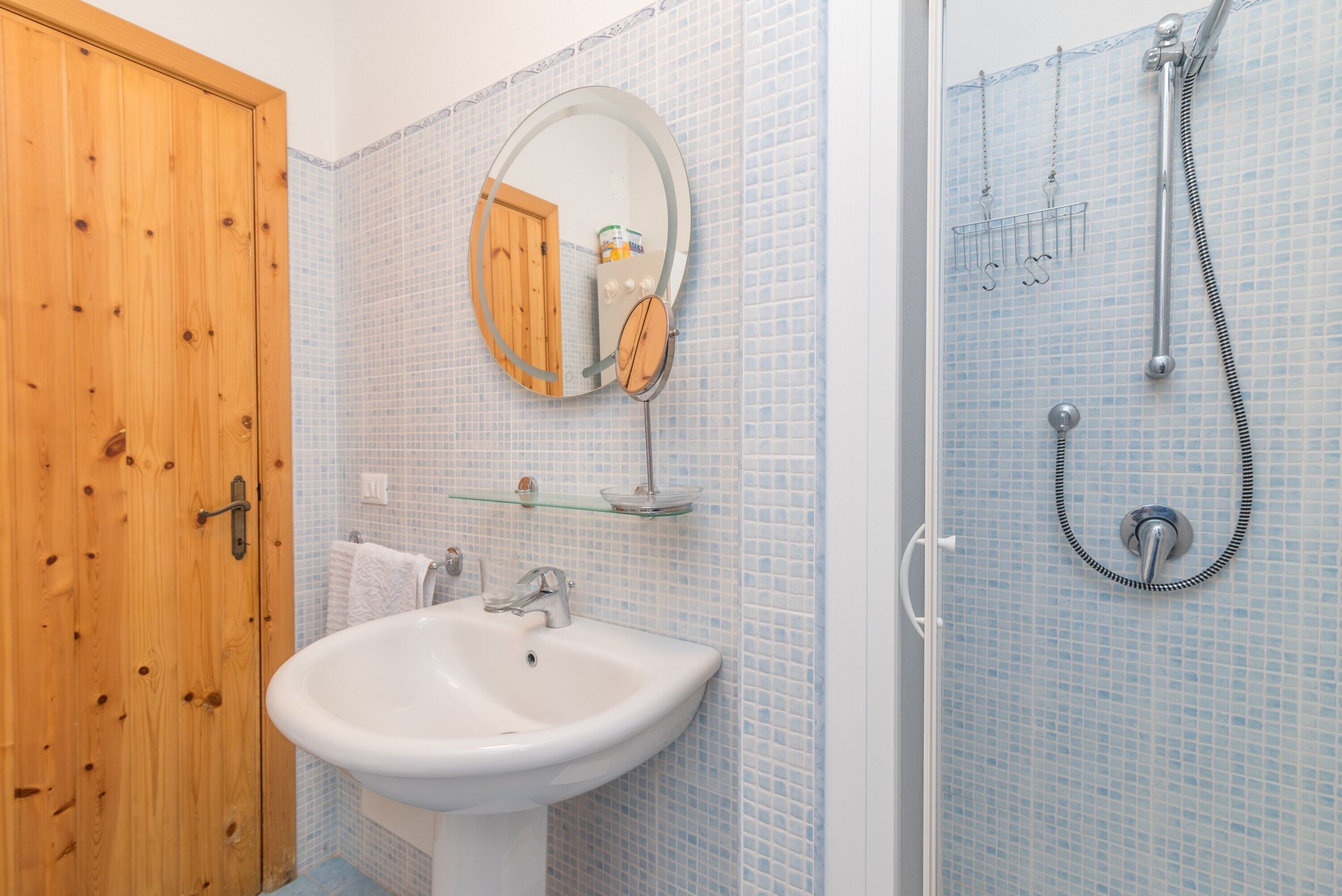 Ein Badezimmer mit Holztür, Waschbecken in Weiß, Spiegel und Dusche mit Glastür.