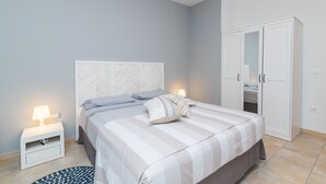 Ein Schlafzimmer mit Bett, Nachttisch, Lampe, Kleiderschrank und einem gemusterten Teppich.