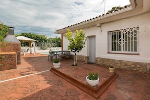 A patio area with a stone floor, a small tree, a table, and a building with a window and a door. - Holiday Home 'Can Fogars' with Sea View, Private Pool and Wi-Fi (fogars de la selva)