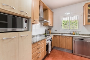 A kitchen with wooden cabinets, a stainless steel microwave, a dishwasher, and a window with a view of greenery. - Holiday Home 'Can Fogars' with Sea View, Private Pool and Wi-Fi (fogars de la selva)
