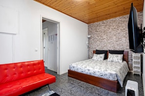 A bedroom with a bed, a red sofa, a brick wall, and a television.
