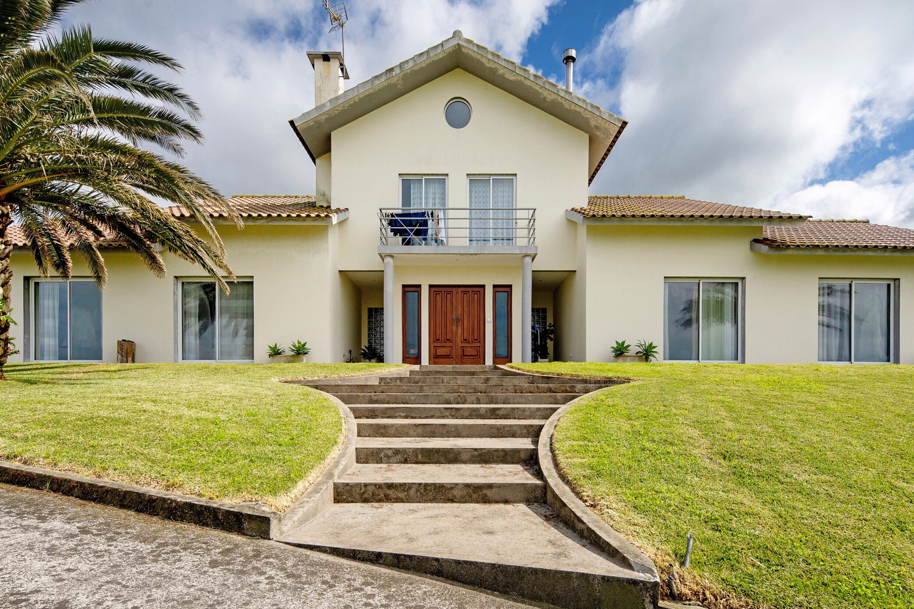 Una casa de dos pisos con un balcón, una puerta principal y una escalera que lleva a la entrada.