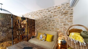 Une pièce chaleureuse avec un mur en pierre, un canapé agrémenté de coussins jaunes, une table en bois et un panier en osier contenant divers objets.