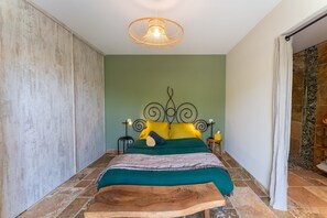 A bedroom with a bed, a wooden headboard, a nightstand, a wall-mounted light fixture, and a shower area. - Holiday Home 'Villa La Mireio' with Private Terrace, Wi-Fi and Air Conditioning (Malaucène)