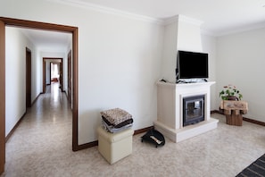 A living room with a fireplace, a television, a hallway, and a small table with a plant. - Villa 'Vivenda Do Monte' with Sea View, Shared Garden and Wi-Fi (Achadinha)