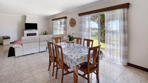 A dining area with a table set for four, surrounded by wooden chairs, a white sofa, and a television on a stand.