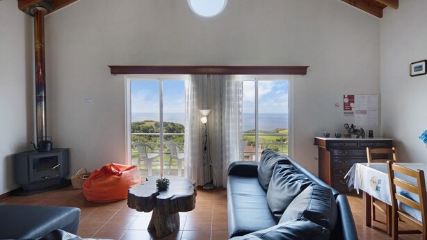 A spacious living area with a sofa, a table, a bean bag, a fireplace, and a view of the outdoors. - Holiday Home 'Casa Do Monte' with Sea View, Shared Garden and Wi-Fi (Achadinha)
