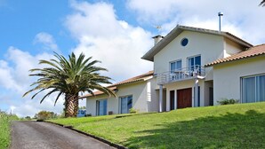 A two-story house with a balcony, a palm tree, and a clear sky. - Holiday Home 'Casa Do Monte' with Sea View, Shared Garden and Wi-Fi (Achadinha)