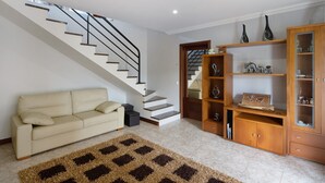 A living room with a staircase, a sofa, a wooden cabinet, and a rug. - Holiday Home 'Casa Do Monte' with Sea View, Shared Garden and Wi-Fi (Achadinha)