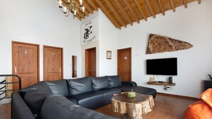 A living room with a sectional sofa, a wooden ceiling, a mounted TV, and a wall-mounted shelf. - Holiday Home 'Casa Do Monte' with Sea View, Shared Garden and Wi-Fi (Achadinha)