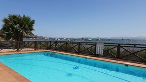 Une piscine avec vue sur les bateaux qui flottent sur l’eau, un palmier et un panneau indiquant les règles.