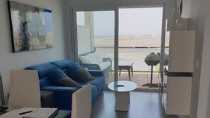 Un salon moderne avec un canapé bleu, une table à manger en verre et une vue sur la plage grâce à de grandes portes coulissantes.