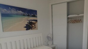 Une chambre à coucher avec un lit, une table de chevet, un tableau représentant une plage et une armoire.
