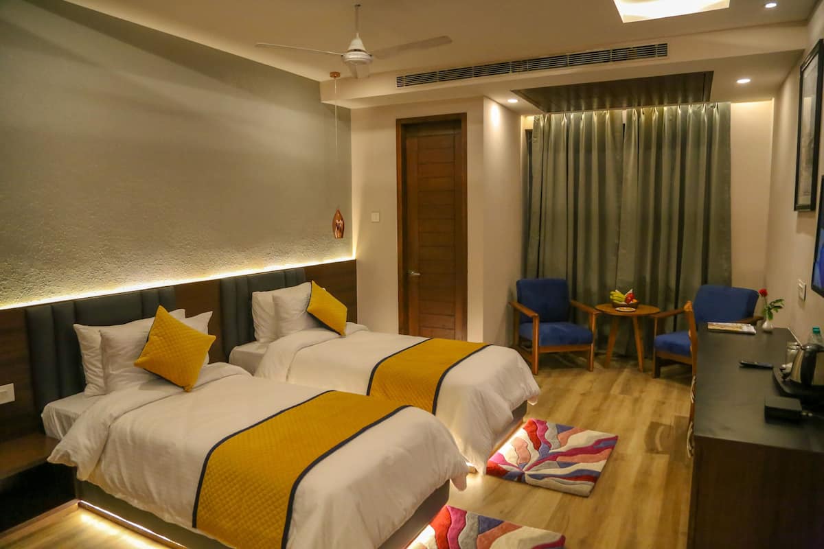 Habitación de hotel con dos camas, un escritorio, una silla, una mesita con fruta y una cortina.
