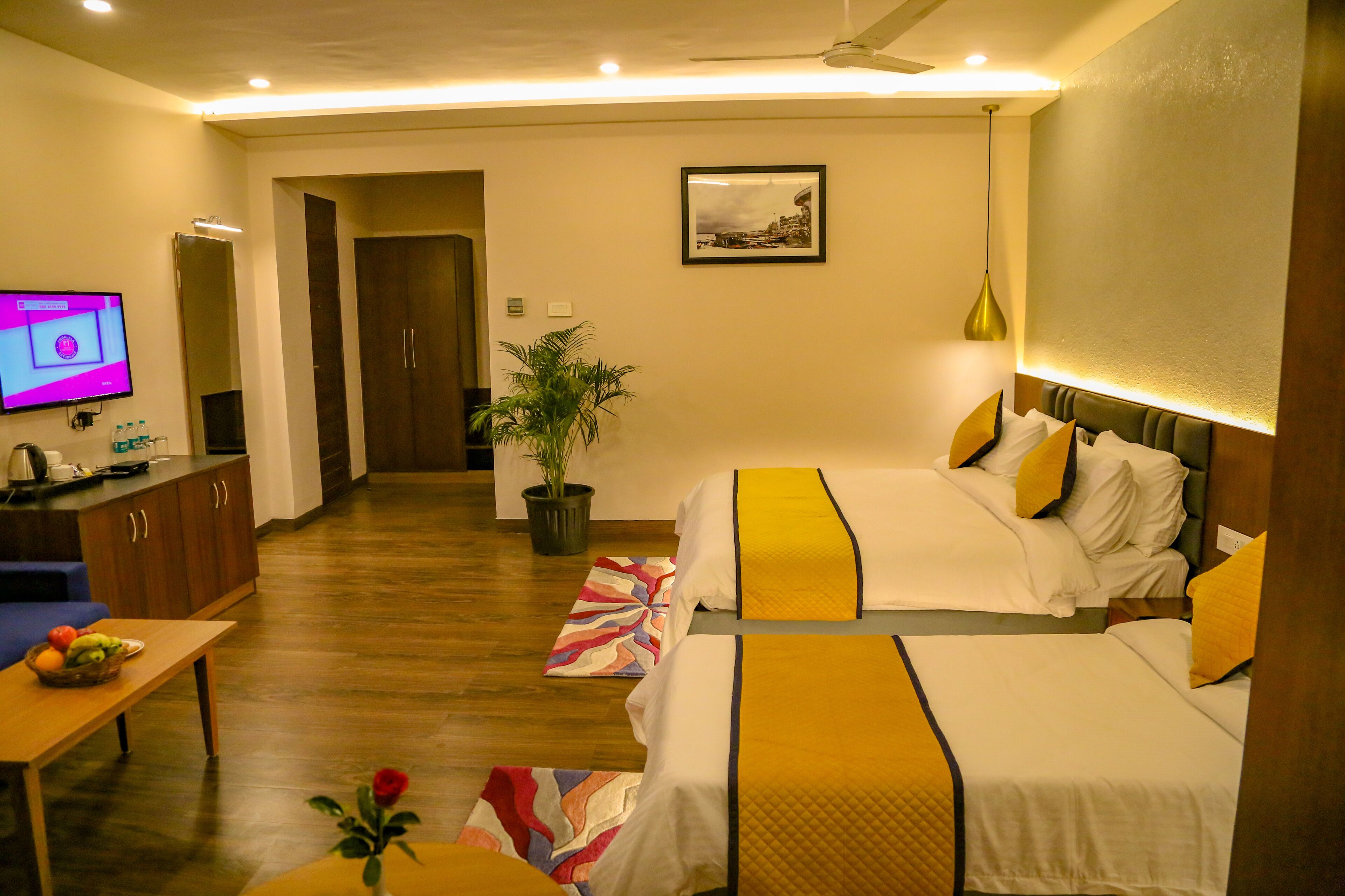 A hotel room with two beds, a desk, a television, and a potted plant.