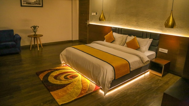 Quarto de hotel moderno com uma cama grande, mesas de cabeceira, uma mesinha e uma poltrona azul.