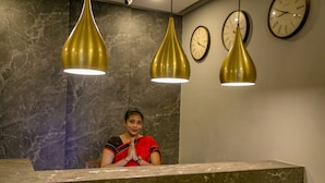 Uma área de recepção com paredes de mármore, um recepcionista e três luminárias pendentes.
